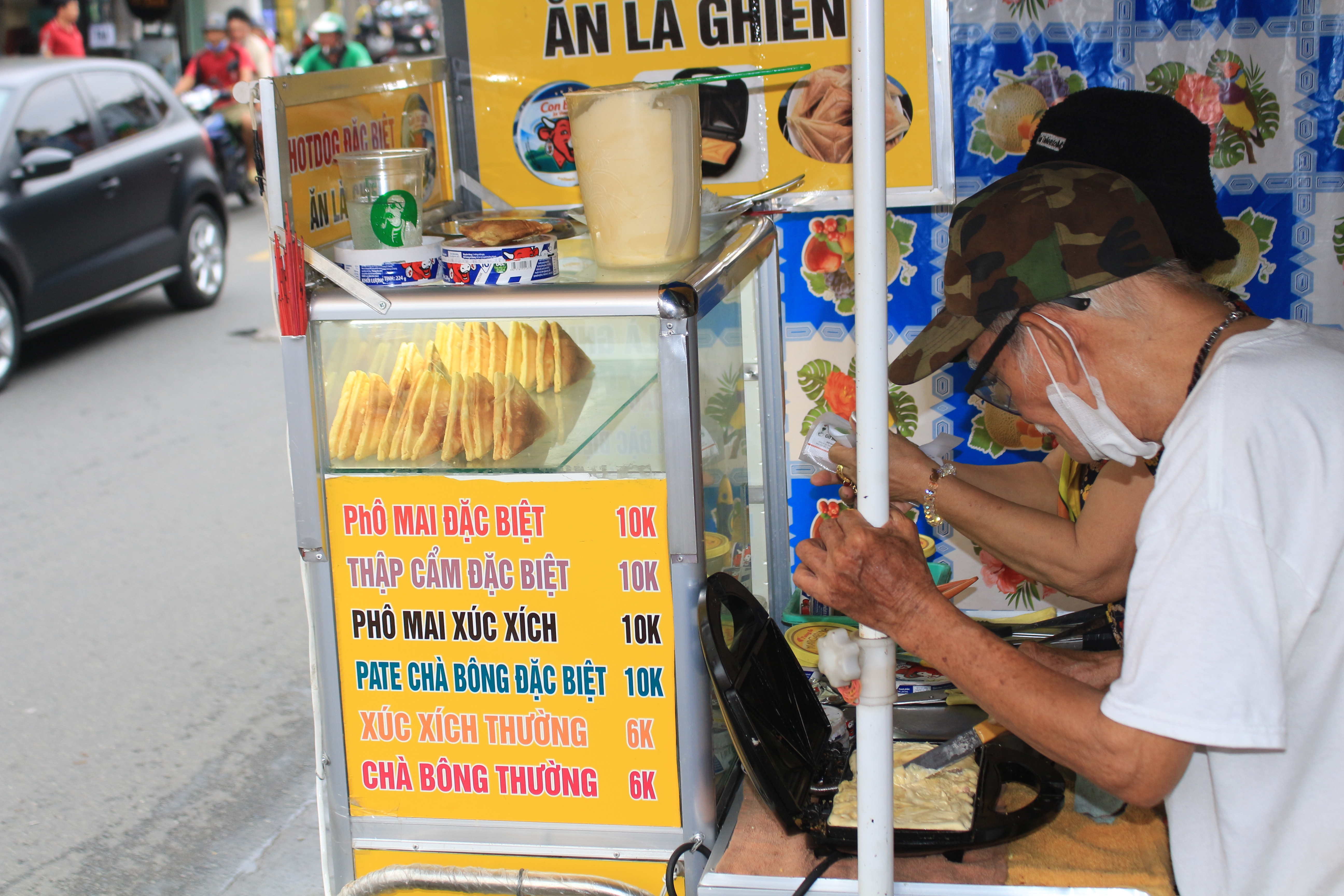 <em>A couple makes Vietnamese-style hot dogs using a toasted sandwich maker on the street in Go Vap District, Ho Chi Minh City. Their cart's menu displays a list of different fillings customers can opt to their liking. Photo: </em>Ray Kuschert / Tuoi Tre News